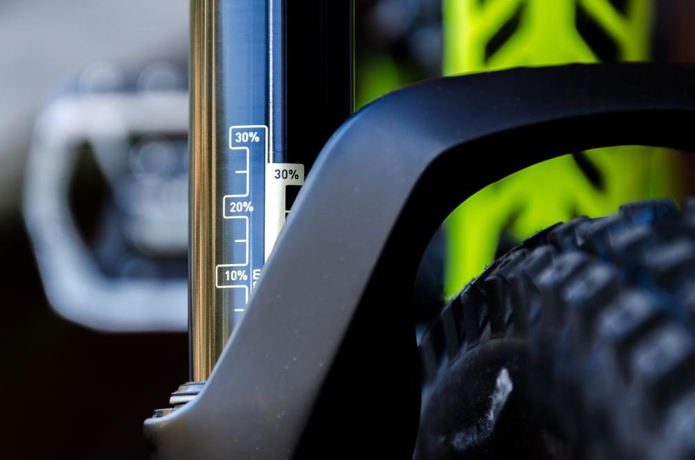 Trek Remedy 7 27.5: Close-up of a bike suspension fork with a visible pressure gauge, indicating 30% on the scale, alongside part of the tire tread and a vibrant green bike frame in the background.