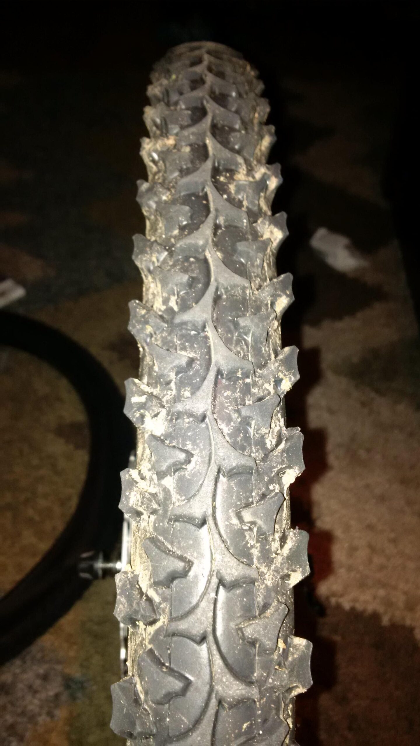 Maxxis C1040N: Close-up view of a worn bicycle tire with a tread pattern designed for off-road cycling, showing dirt and debris on the surface.