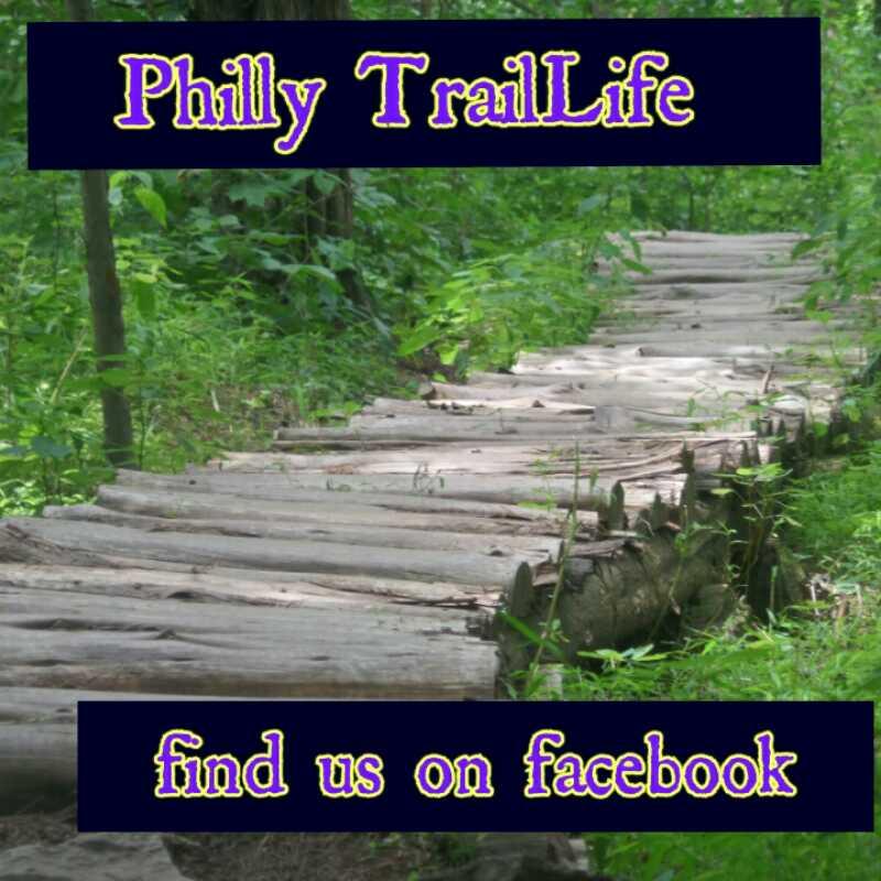 A wooden pathway winding through a lush green forest, accompanied by text that reads "Philly TrailLife" and "find us on facebook" at the top and bottom of the image. Green Lane mountain bike trail.