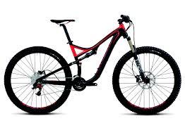 Specialized Stumpjumper FSR Comp 29: A modern mountain bike with a black and red frame, featuring thick tires and a front suspension fork. The bike is positioned in profile view, showcasing its sleek design and robust features suitable for off-road trails.
