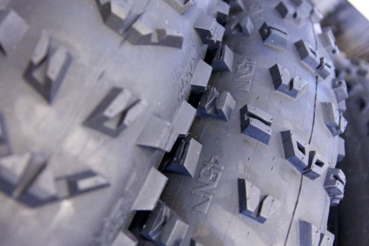 Close-up of two patterned tires stacked next to each other, showcasing the tread design and rubber texture against a blurred wooden background.