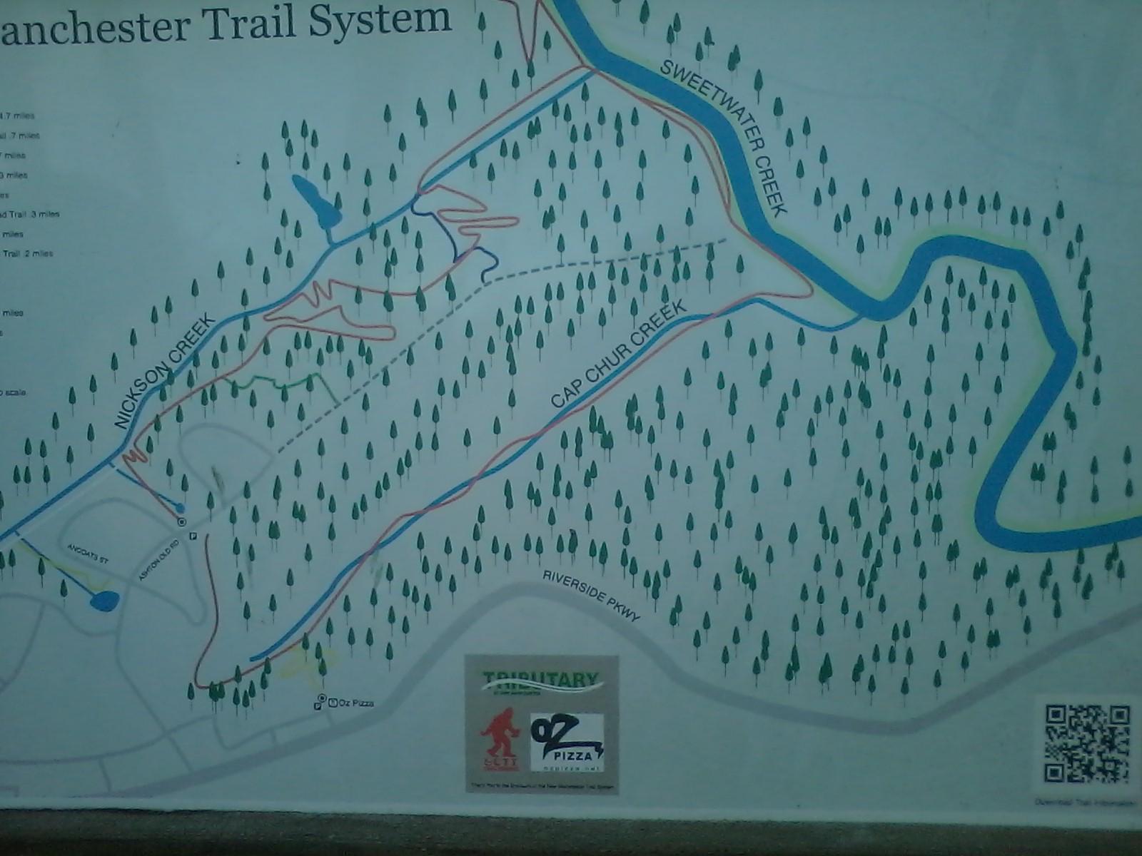 Map of the Manchester Trail System, featuring trails labeled with different colors, surrounding creeks like Nickson and Sweetwater, and various pine trees. Additional information includes distances for each trail segment and a QR code for further details. Tributary mountain bike trail.