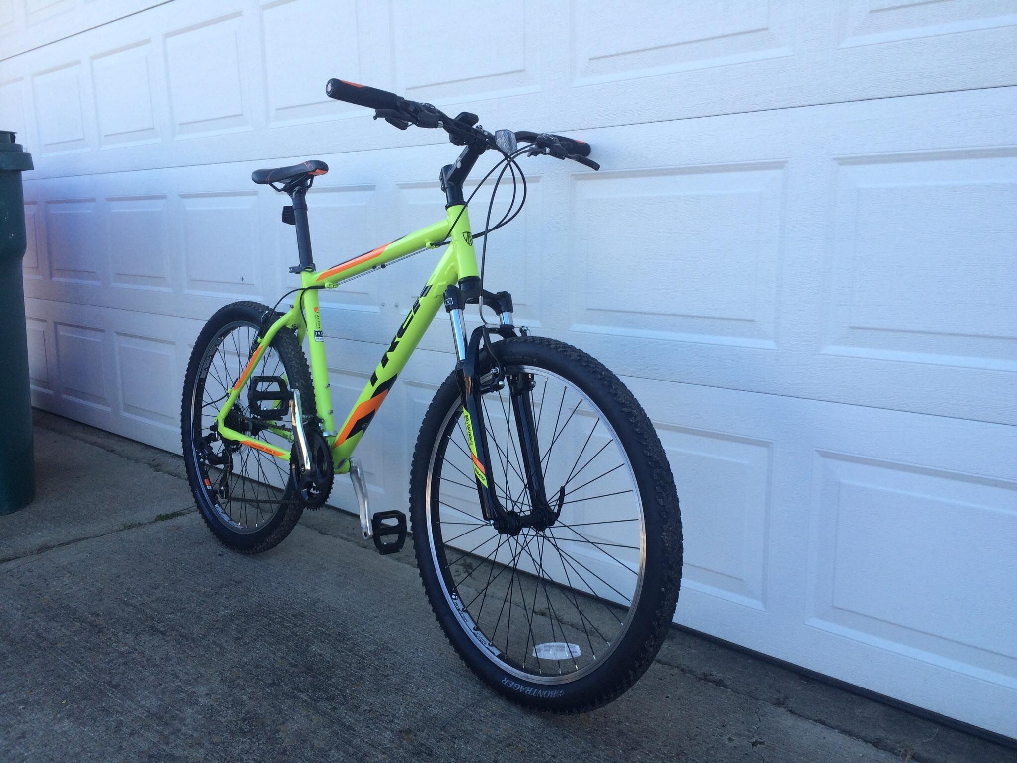 Trek 3500: A bright green and orange mountain bike leaning against a garage door, featuring large tires and a lightweight frame. A trash can is visible in the background. The bike is positioned in a way that showcases its design and details.