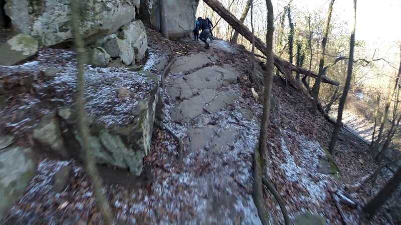 A hiker navigating a rocky trail surrounded by trees, with some patches of snow and fallen leaves on the ground. Buttermilk mountain bike trail.