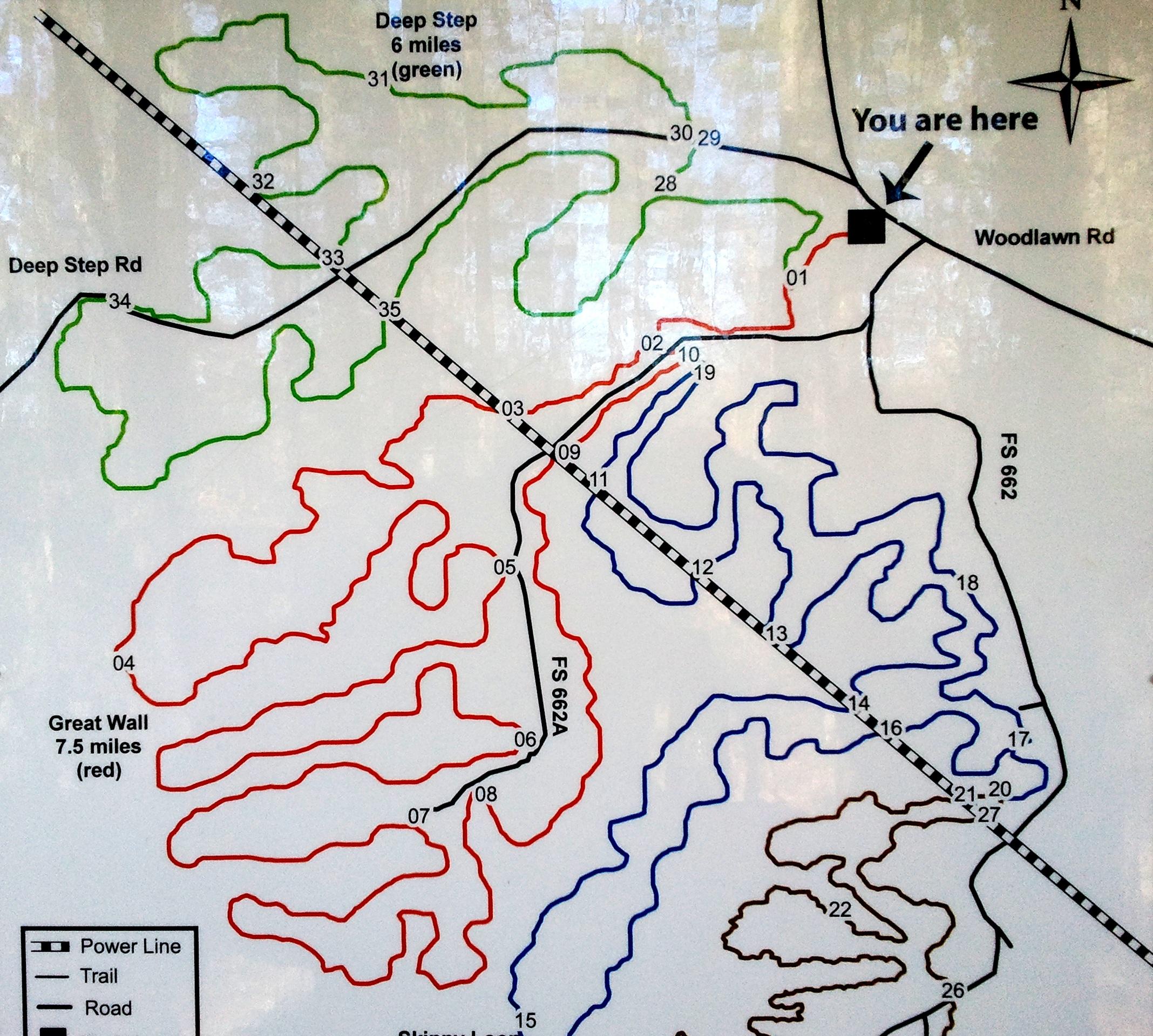 Map of a hiking or trail area showing different routes and landmarks. Key features include color-coded lines representing various trails: green for Deep Step, red for Great Wall, and blue for other paths. The map indicates the viewer's current location with a marker labeled "You are here," along with nearby roads such as Woodlawn Rd. North orientation is marked with a compass symbol. Forks Area Trail System (FATS) mountain bike trail.