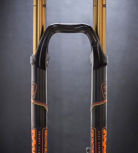 A close-up image of a mountain bike fork with a black and gold design. The fork features dual suspension components, highlighted by the gold upper tubes and black lower sections adorned with colorful branding. The background is a soft gradient, enhancing the sleek appearance of the fork.