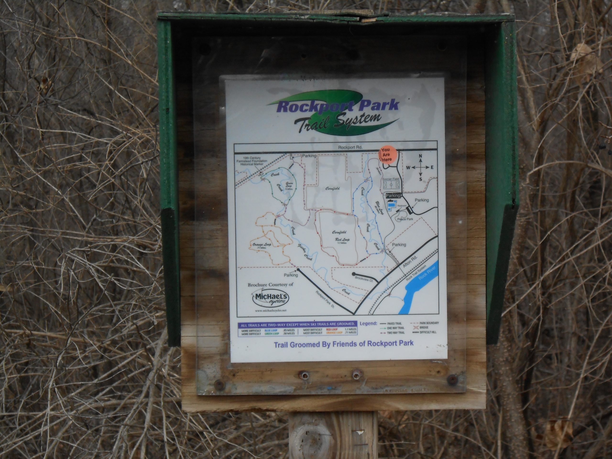 Map of the Rockport Park Trail System, displayed in a wooden kiosk, indicating trails, parking areas, and the "You Are Here" location. The map is surrounded by sparse vegetation, suggesting a natural setting. Rockport Park MTB mountain bike trail.