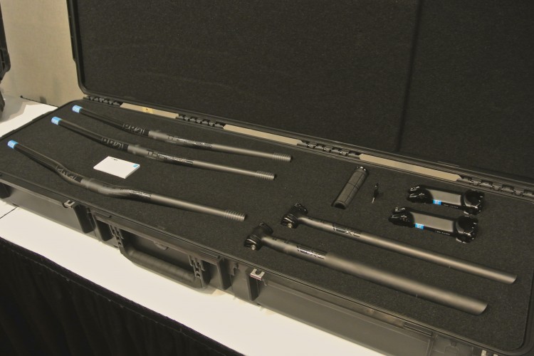 A closed black case with foam padding displaying various bike components, including several handlebars, a grip, and two stem pieces. The components are primarily black with blue accents and are neatly organized inside the case.