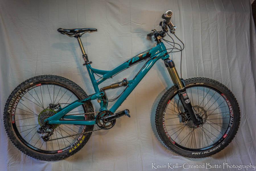 Yeti SB66: A teal mountain bike is displayed against a neutral background. The bike features thick tires, front suspension, and a modern frame design, showcasing its readiness for off-road trails and rugged terrain.