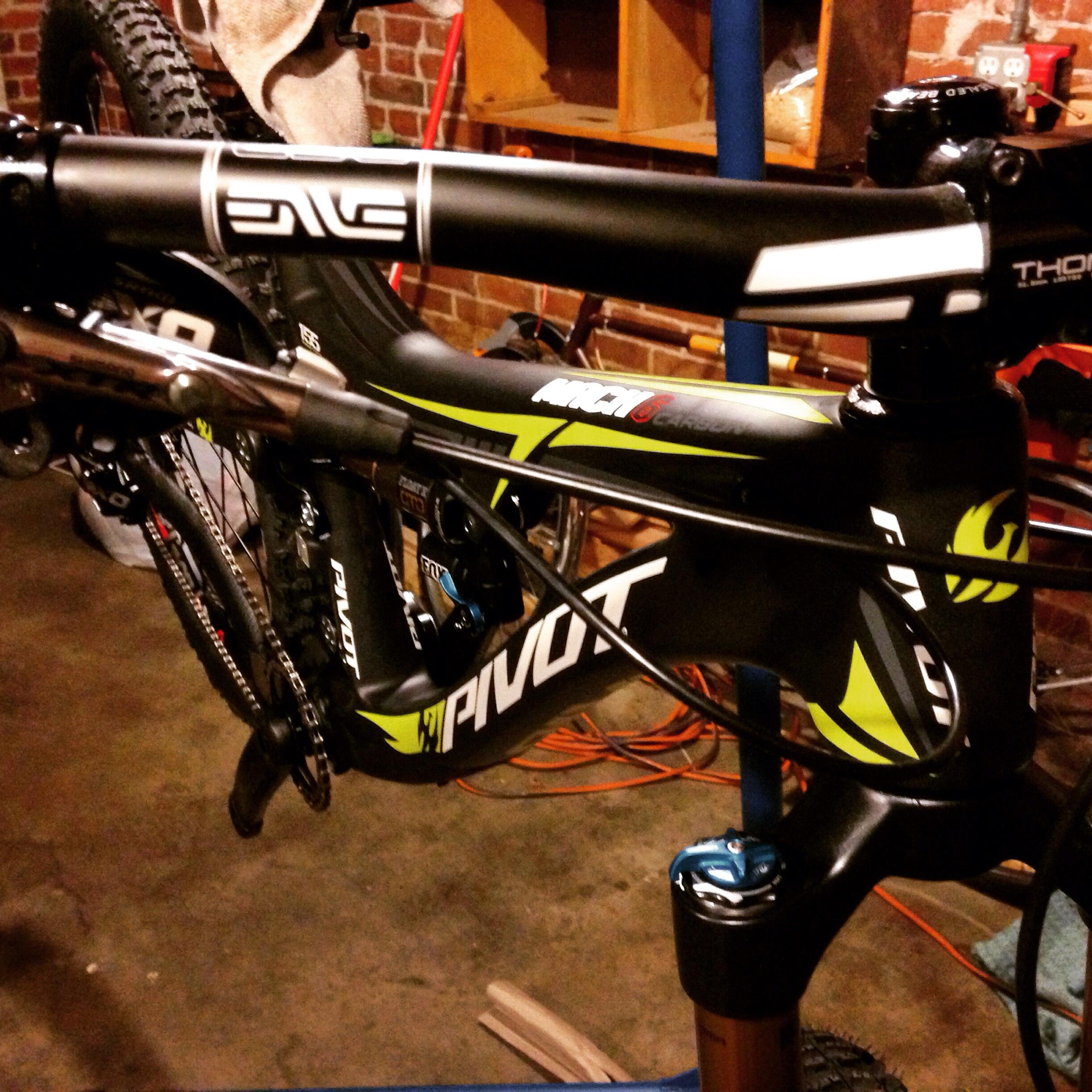 Pivot Mach 6: Alt tag: Close-up of a black and green mountain bike frame on a workstand, showcasing the handlebar, stem, and various components in a garage setting.