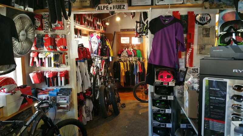 Interior view of a bicycle shop showcasing a variety of biking gear, including helmets and jerseys hanging on walls. Bicycles are placed throughout the space, and shelves display various accessories, creating an inviting atmosphere for cycling enthusiasts.