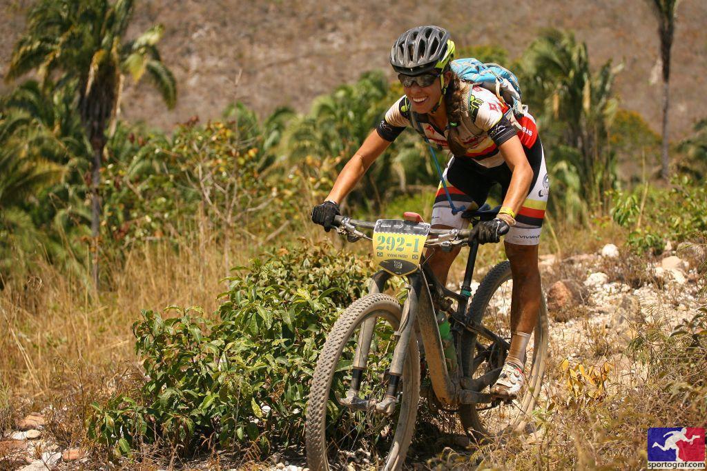 Specialized S-Works Era FSR Carbon: A mountain biker, wearing a colorful jersey and helmet, navigates a rocky terrain with lush greenery in the background. The cyclist is focused and determined, showcasing the challenge of the outdoor trail.