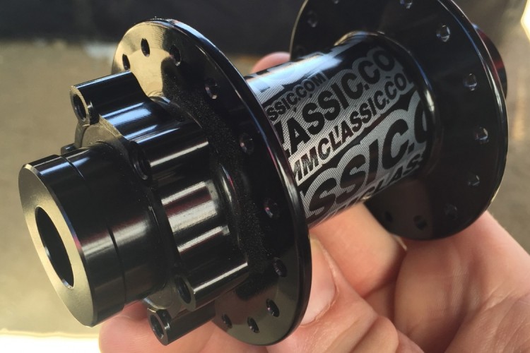 Close-up of a black bicycle hub held in a hand, featuring a shiny surface and multiple holes for spokes, with branding visible on the side.