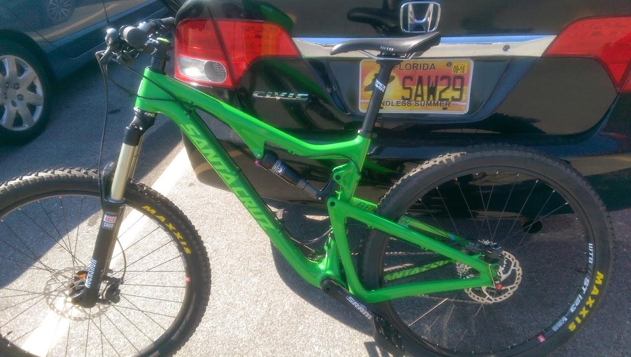 Santa Cruz Bronson: A bright green Santa Cruz mountain bike parked beside a black Honda Civic, with clear visibility of the bike
