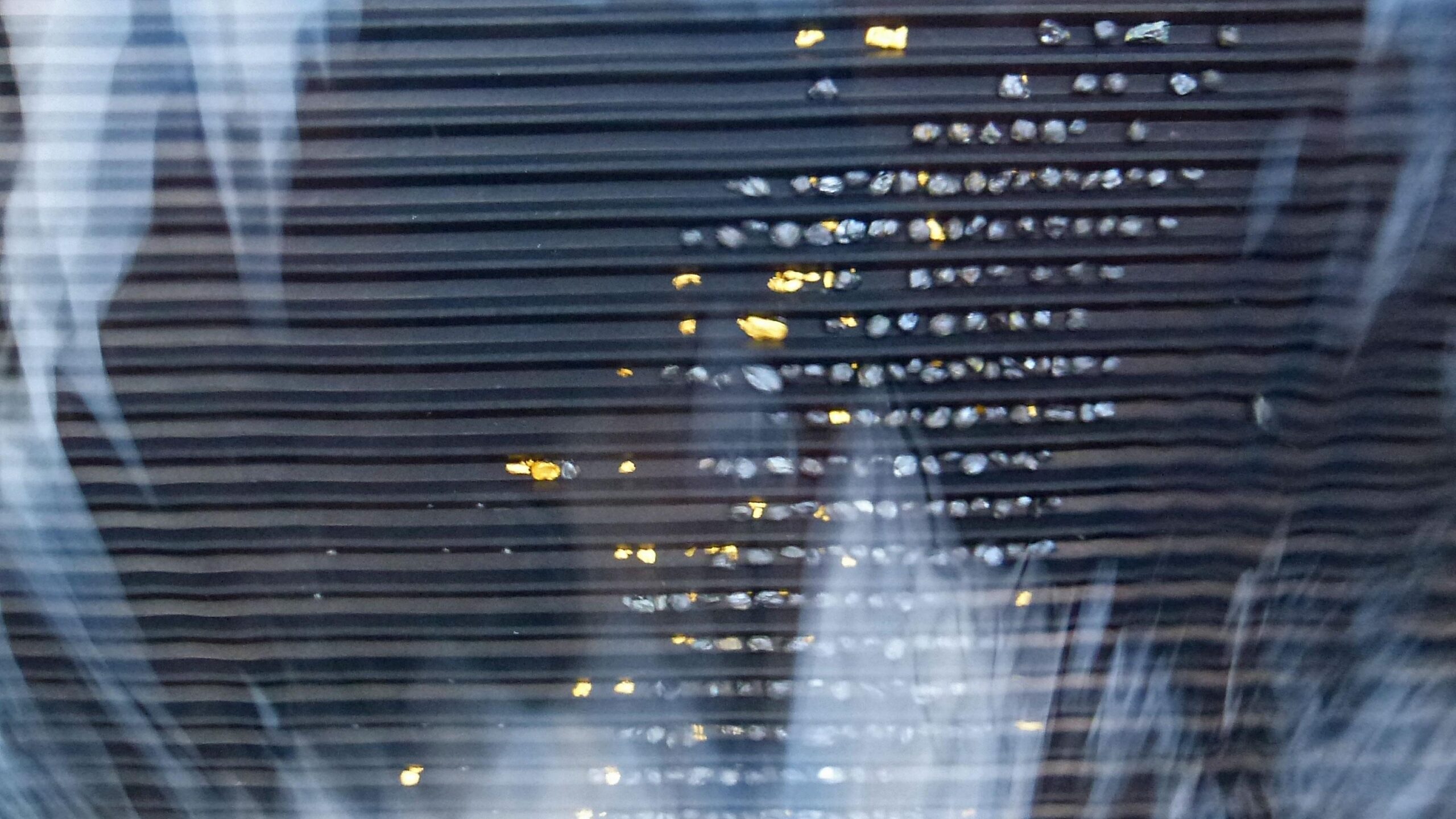 Close-up view of a textured surface with horizontal lines, featuring reflections of light that create a shimmering effect. Small bright spots appear interspersed among the lines, adding visual interest to the image. Macetown and the Arrow Gorge mountain bike trail.
