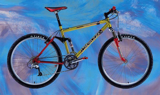 Kona MokoMoko: A vibrant mountain bike with a bright yellow frame and red accents, displayed against a colorful abstract background. The bike features rugged tires, a visible gear system, and a comfortable seat, showcasing its design for off-road adventures.