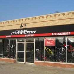 Front view of a bike shop named "Cycle Connection," showcasing large glass windows displaying various bicycles for sale. The storefront features signage indicating "Sales," "Service," and "Accessories," with a red and black color scheme.