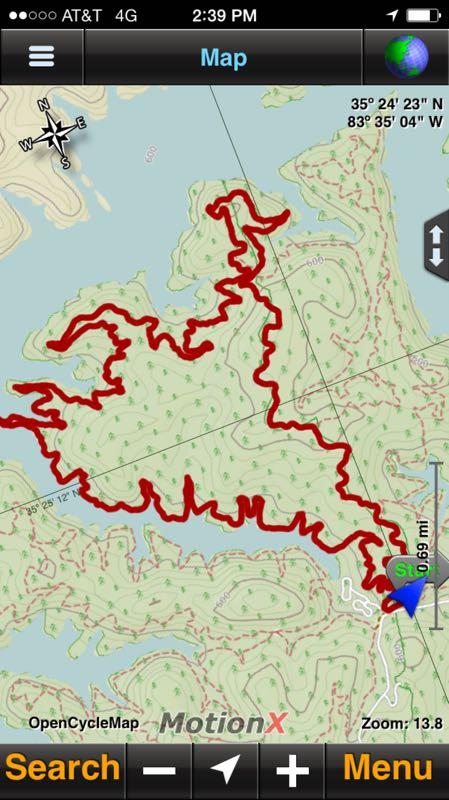 Map showing a topographic trail outline in red on a green background, indicating elevation changes and terrain features. The map includes location coordinates, a directional compass, and a navigation marker in the bottom right corner. Santos mountain bike trail.