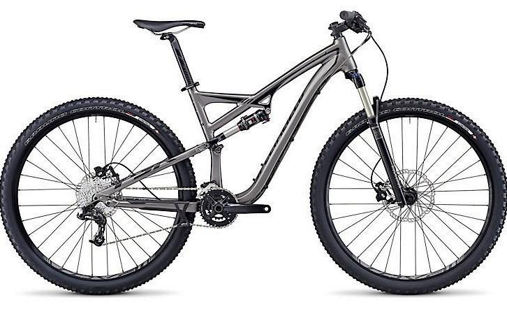 Specialized Camber Comp 29: A modern mountain bike with a sleek gray frame, front suspension, and thick tires designed for off-road riding. The bike features a dual suspension system, disc brakes, and a complete set of gears for varied terrain.
