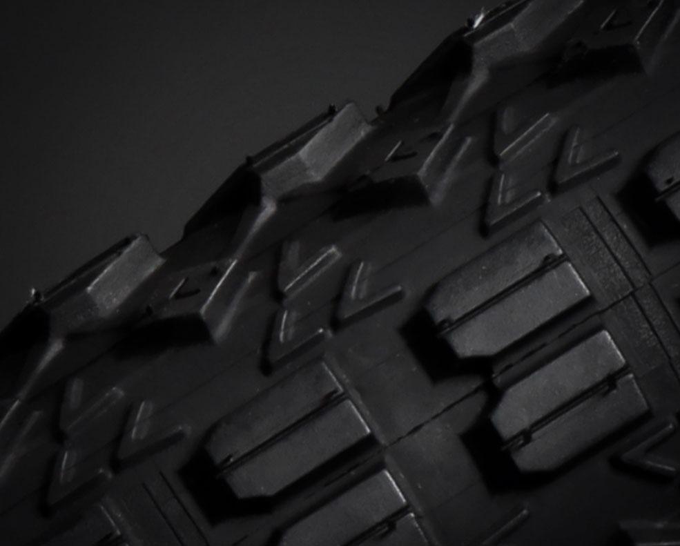 Vee Rubber Trax Fatty: Close-up view of a textured black rubber tire tread against a dark background.