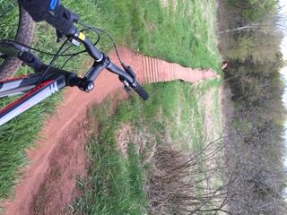 Giant Talon 27.5: A close-up view of a mountain bike parked beside a winding dirt trail, surrounded by greenery. The trail appears narrow and is bordered by grass and brush, leading into the distance.