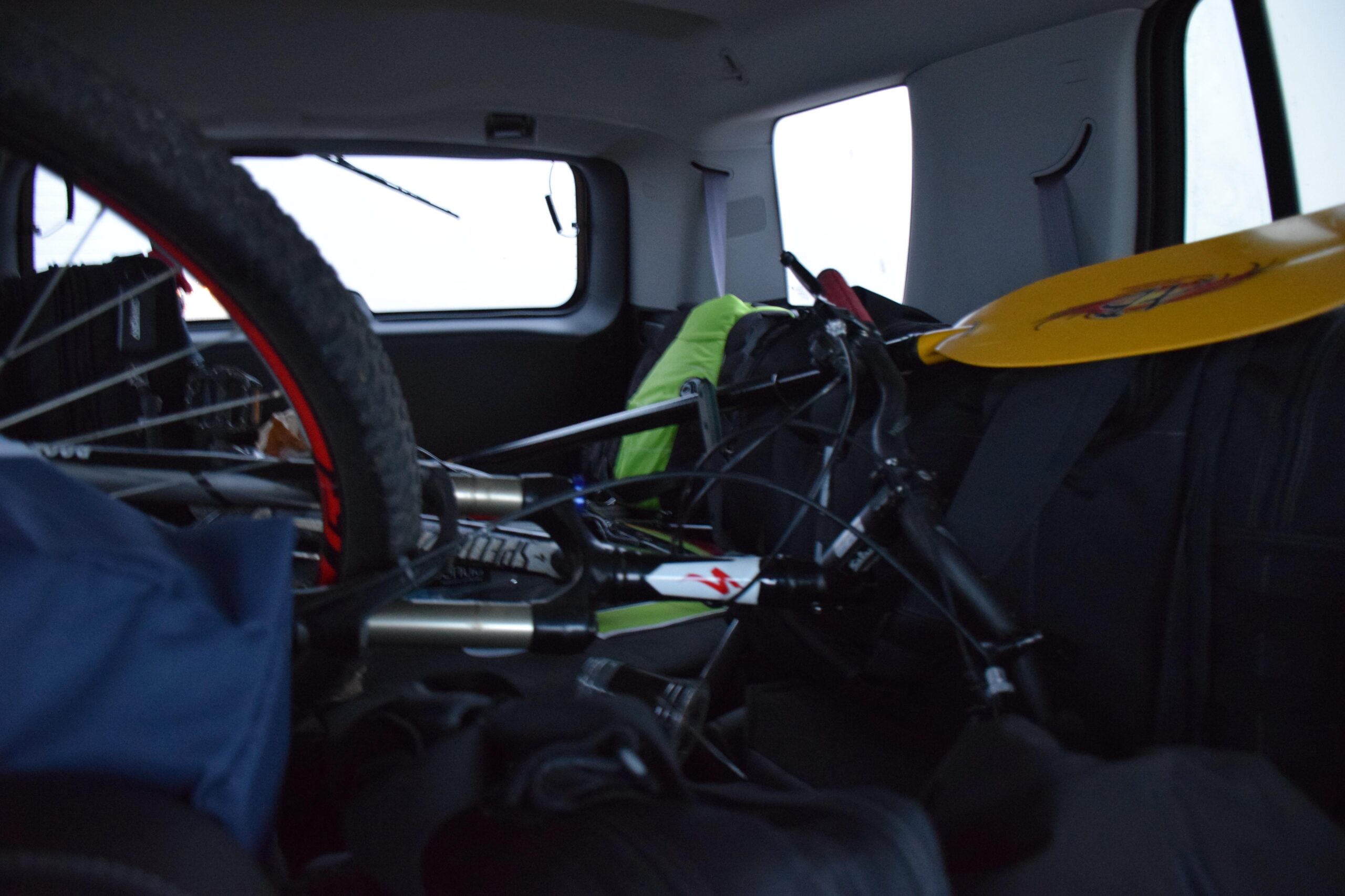 Specialized Hardrock Sport Disc 29er: A cluttered interior of a vehicle showing various items including a bicycle, bags, and an item resembling a yellow kayak paddle. The image captures an organized chaos typical of an outdoor adventure or road trip setup.