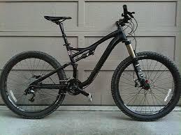 Specialized Stumpjumper: A black mountain bike leaning against a garage door, featuring thick tires and a suspension system, designed for off-road cycling.