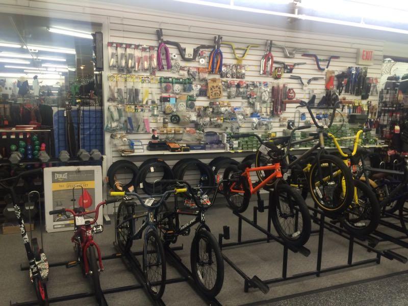 A display inside a bicycle shop featuring a variety of bikes for sale, including BMX and children's models, along with an assortment of bicycle parts and accessories mounted on a wall behind them.