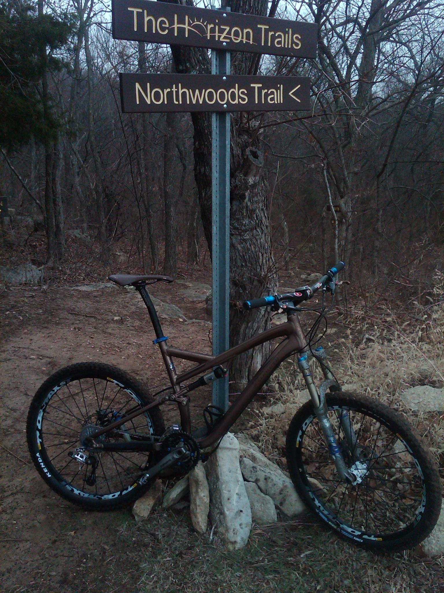 Specialized Stumpjumper FSR Expert: A mountain bike resting near a trail sign for The Horizon Trails and Northwoods Trail, surrounded by trees and dry grass.