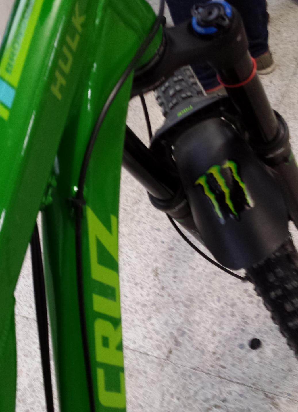 Santa Cruz Bronson: Alt text: A close-up of a bright green mountain bike showing the brand name "Cruz" and the word "HULK" on the frame, with a visible suspension fork featuring a black cover adorned with the Monster Energy logo.
