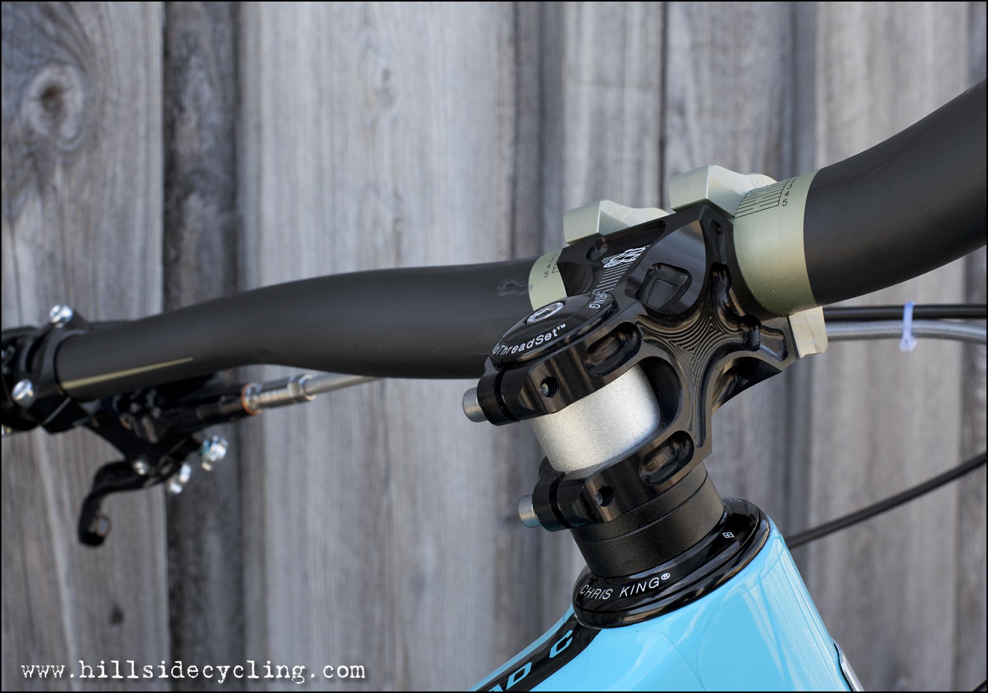 Santa Cruz Nomad Carbon 27.5: Close-up image of a bicycle's handlebars and stem featuring a black and silver headset and black handlebar, with a wooden background.