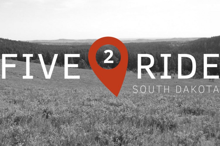 A scenic view of a meadow and hills with the text "FIVE 2 RIDE SOUTH DAKOTA" overlaid. The design features a red location pin around the number 2, suggesting a theme of exploration or adventure in South Dakota. The image is predominantly in black and white, highlighting the vastness of the landscape.