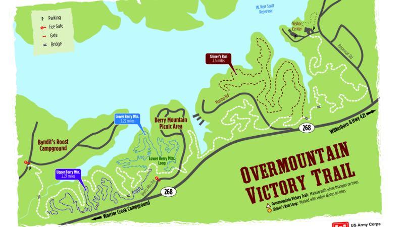 Map of the Overmountain Victory Trail, featuring key locations such as parking areas, campgrounds, and hiking trails. Notable points include Bandit's Roost Campground, Berry Mountain Picnic Area, and Shiner's Run Trail. Routes and distances to various destinations are indicated, along with symbols for fees and access. The map also highlights surrounding bodies of water and access roads. Kerr Scott Trails mountain bike trail.
