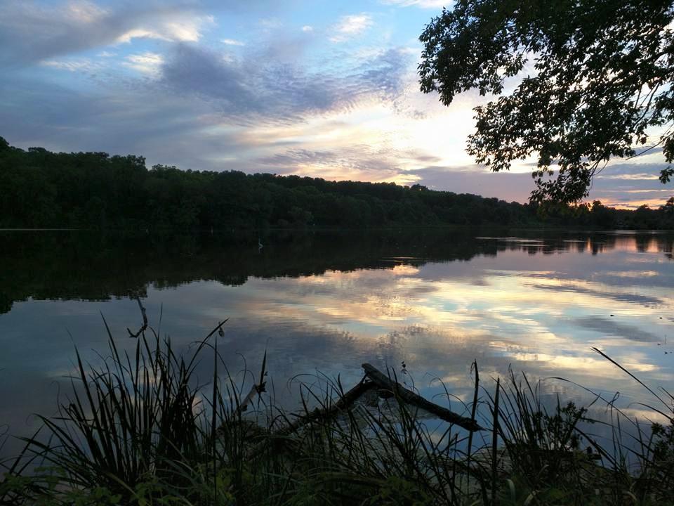 A tranquil lake at sunset, with reflections of colorful clouds and trees on the water