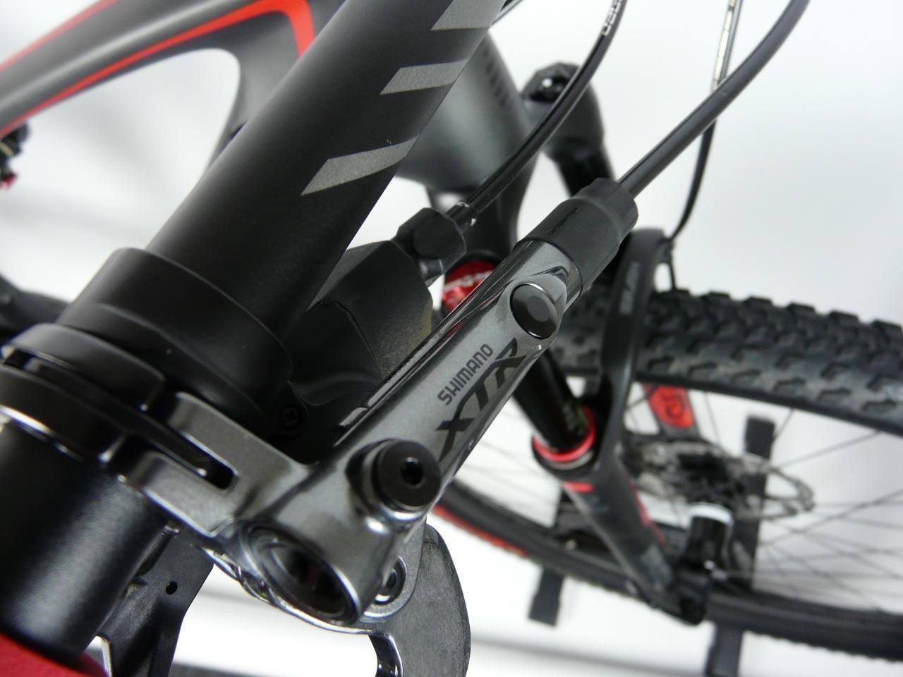 Specialized Epic Expert Carbon 29er: Close-up view of a bicycle's brake system, featuring a Shimano XTR brake component. The image highlights the sleek design of the bike's frame and the detailed mechanical elements, with a focus on the connection between the brake lever and the frame. The background is neutral to emphasize the bike parts.
