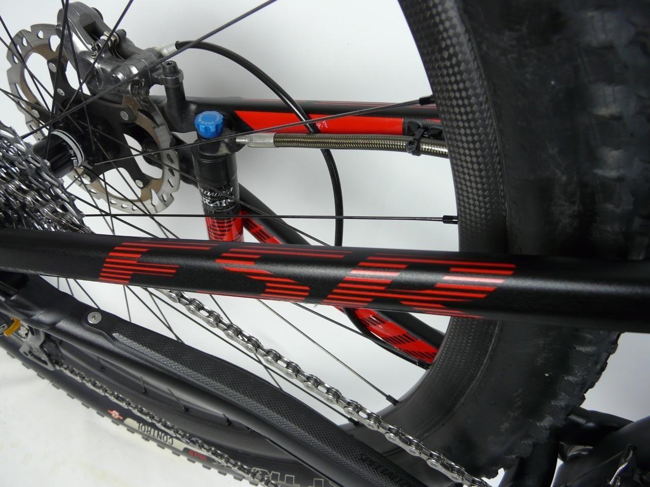 Specialized Epic Expert Carbon 29er: Alt text: Close-up view of a bicycle frame featuring a black finish with red accents, highlighting the chain, brake disc, and tire.