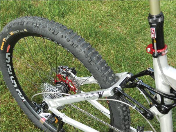 Knolly Chilcotin: Close-up view of a mountain bike's rear wheel and suspension system, showcasing the tire's tread pattern and the bike's frame details against a grassy background.