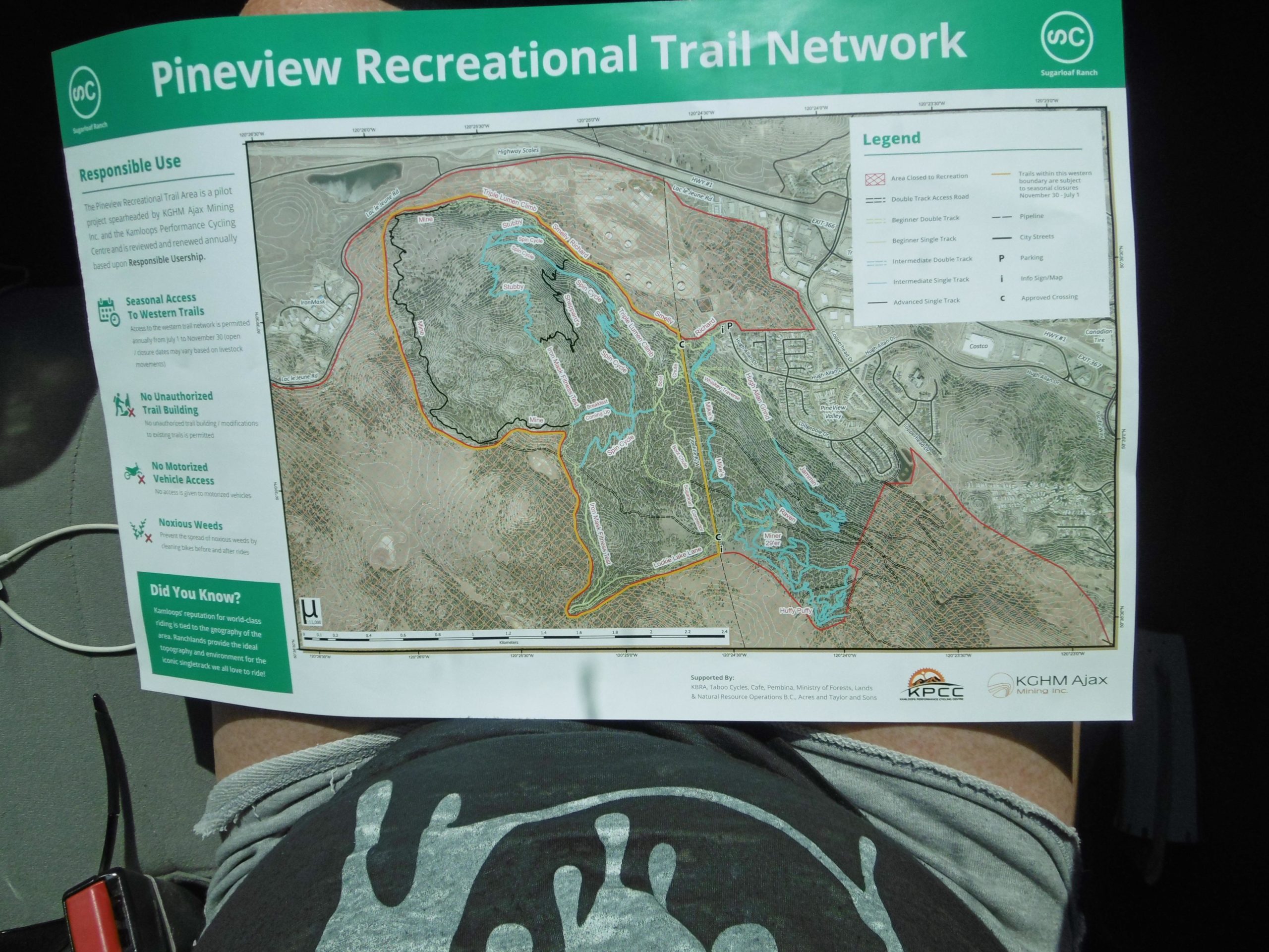 Map of the Pineview Recreational Trail Network, featuring trails for different skill levels, including trails closed to recreation, a legend, and guidelines for responsible trail use. The map is held by an individual's legs in a seated position. Pineview mountain bike trail.