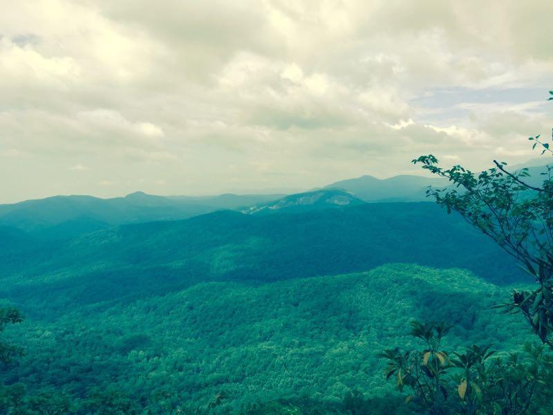 A panoramic view of lush green mountains under a partly cloudy sky, showcasing layered hills and valleys in the distance. Black Mountain mountain bike trail.