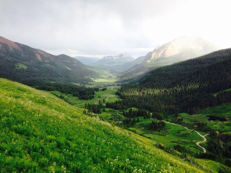 A scenic landscape view of a lush green valley surrounded by mountains, with a winding dirt road through the meadows. Soft clouds hover in the sky, casting gentle light over the picturesque terrain. Trail 401 mountain bike trail.