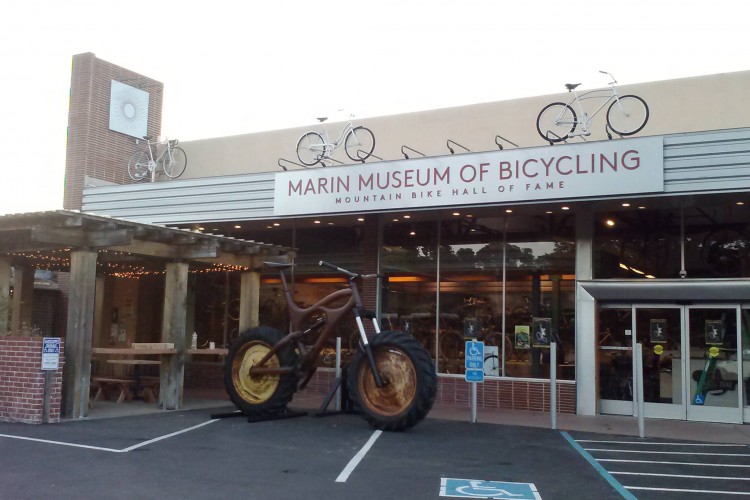 Alt text: "Exterior view of the Marin Museum of Bicycling, featuring a large bicycle sculpture at the entrance, a sign reading 'Marin Museum of Bicycling' and 'Mountain Bike Hall of Fame', and decorative bicycles mounted on the building."