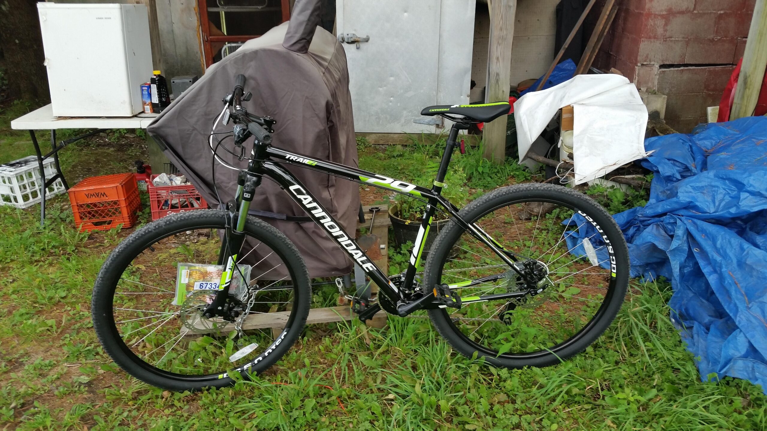 Cannondale Trail: A black and green Cannondale mountain bike parked on grass, with a table and various items in the background, including a fridge and tarps.