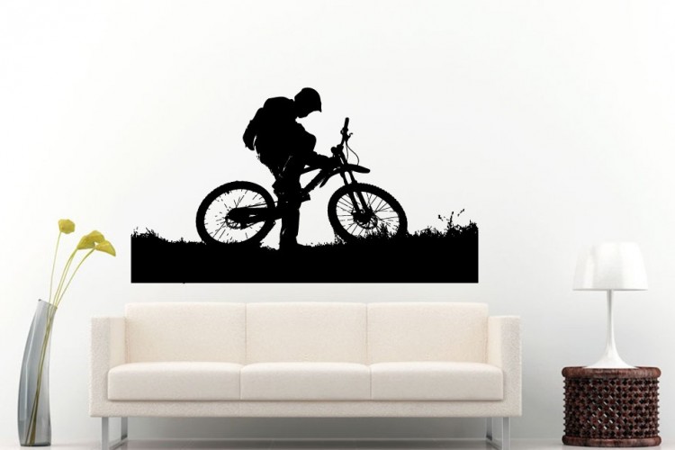 Silhouette of a person leaning over a bicycle, set against a simple wall background. The scene features grass at the bottom, creating a playful and adventurous atmosphere. A light-colored couch and a floor lamp are visible in the foreground, adding to the living space setting.