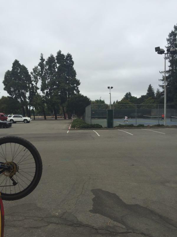 A view of a partially empty parking lot with a bicycle wheel in the foreground. In the background, there