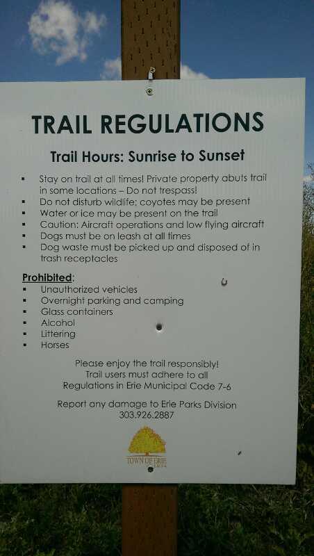 Sign displaying trail regulations including hours of operation, safety precautions, and prohibited items for trail use. Instructions emphasize staying on the trail, respecting wildlife, and responsible pet ownership. Prohibited items listed include unauthorized vehicles, camping, glass containers, alcohol, littering, and horses. The sign provides contact information for reporting issues. Sunset East mountain bike trail.