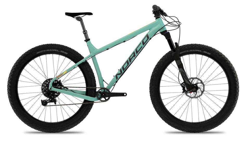 Norco Torrent 7: A teal-colored mountain bike with a sturdy frame, large knobby tires, and a sleek design, featuring front suspension and a single front chainring. The bike is positioned on a white background, showcasing its lightweight build and modern components.