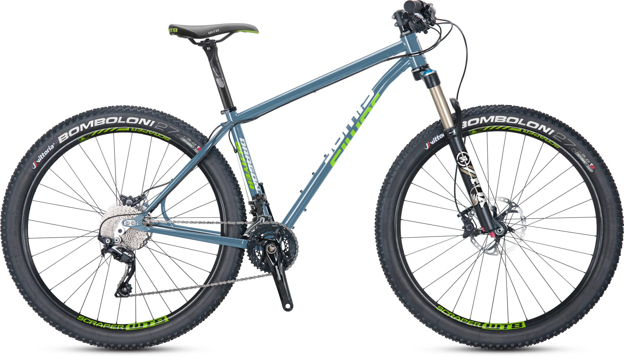 Jamis Dragonslayer 27.5: A mountain bike with a lightweight blue frame, featuring wide tires with "BOMBOLONI" branding. The bike is equipped with disc brakes and a combination of Shimano and Vittoria components, showcasing a modern design aimed for off-road cycling. The seat is positioned upright, and the handlebars are slightly raised for a comfortable riding posture.