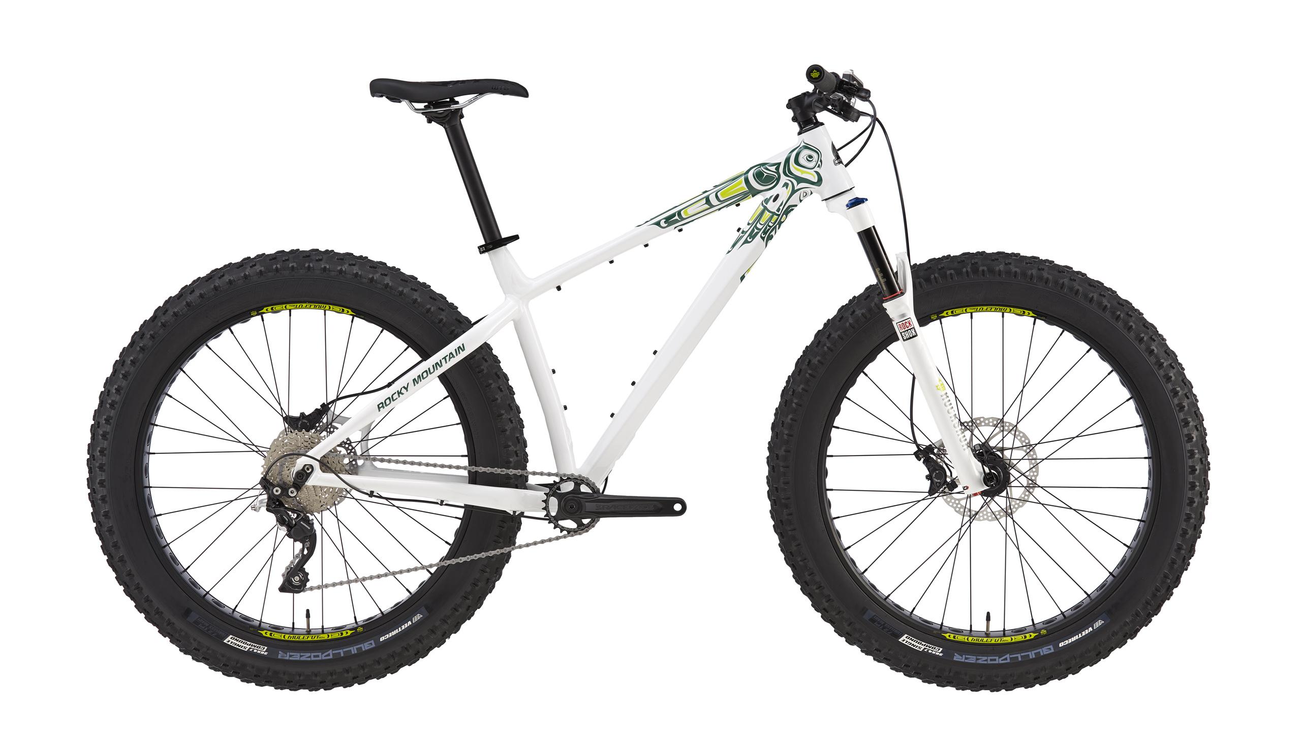 A white fat bike with large, knobby tires, featuring a sleek frame and minimalistic design. The bike includes a front suspension fork, disc brakes, and a gear system visible on the rear wheel. The frame is decorated with subtle green and yellow graphics, and it is positioned against a plain background.