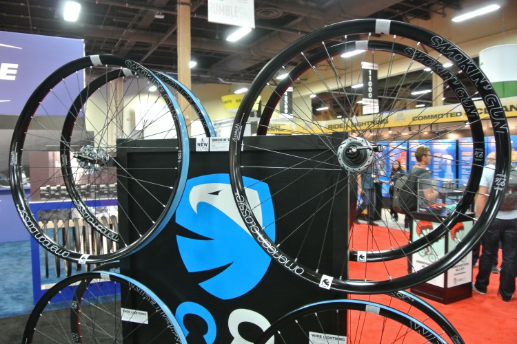 Alt text: Display of bicycle wheels featuring various models and designs at an indoor exhibition, with a colorful background and attendees in the distance.
