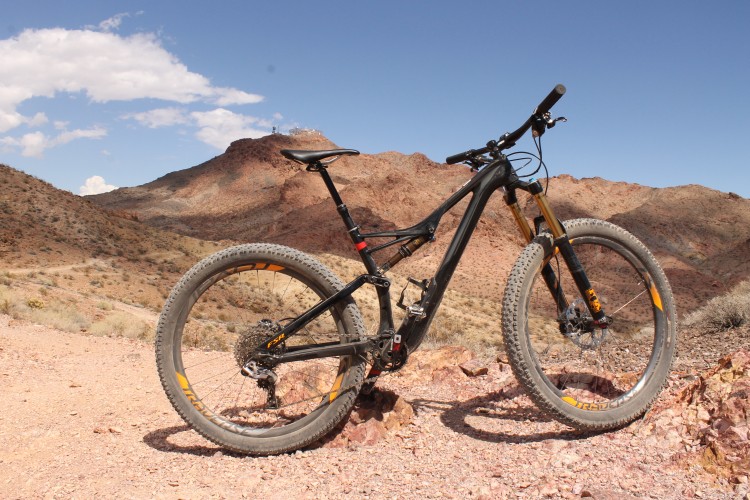 A mountain bike parked on rocky terrain with red mountains in the background under a clear blue sky.